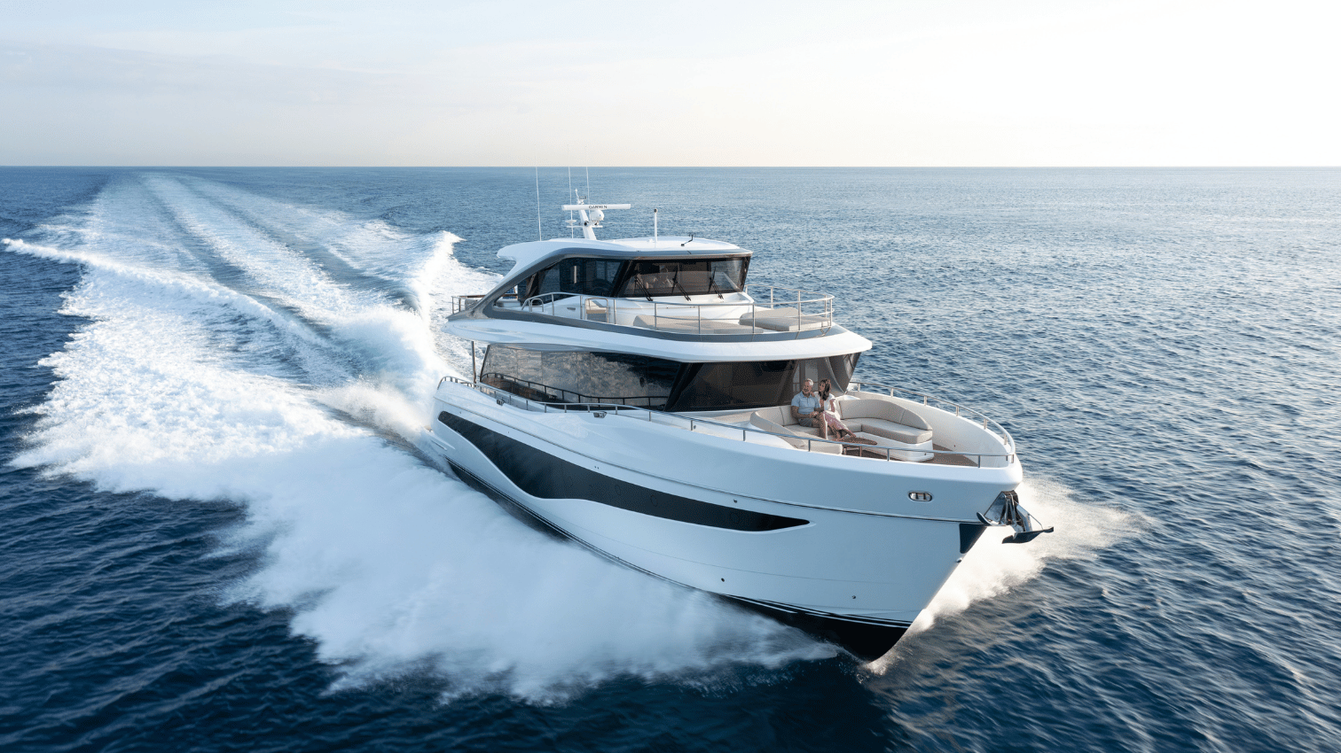 A Princess X80 Yacht running on the open water with a couple sitting down on the forward seating in the front of the boat.